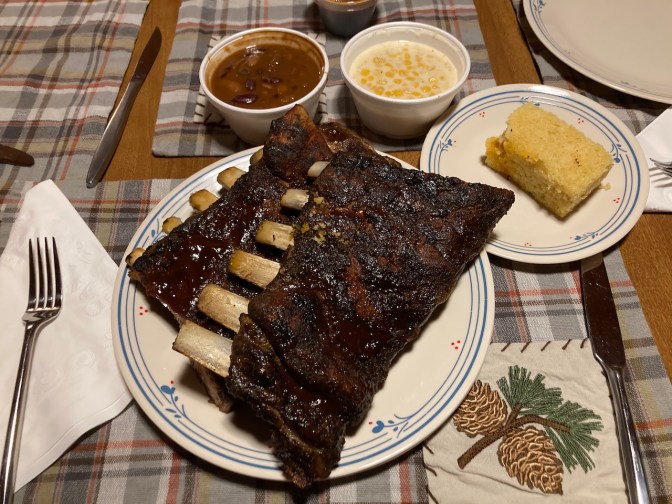 Plates with barbecue ribs, cornbread, and sides of creamed corn and baked beans.