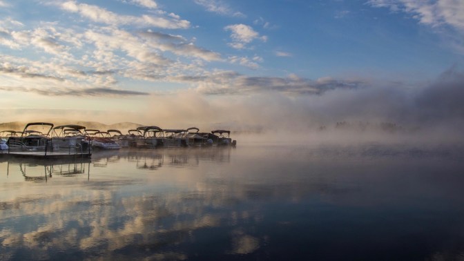 Fog over Fourth Lake, with boats tied to dock on left side of image.
