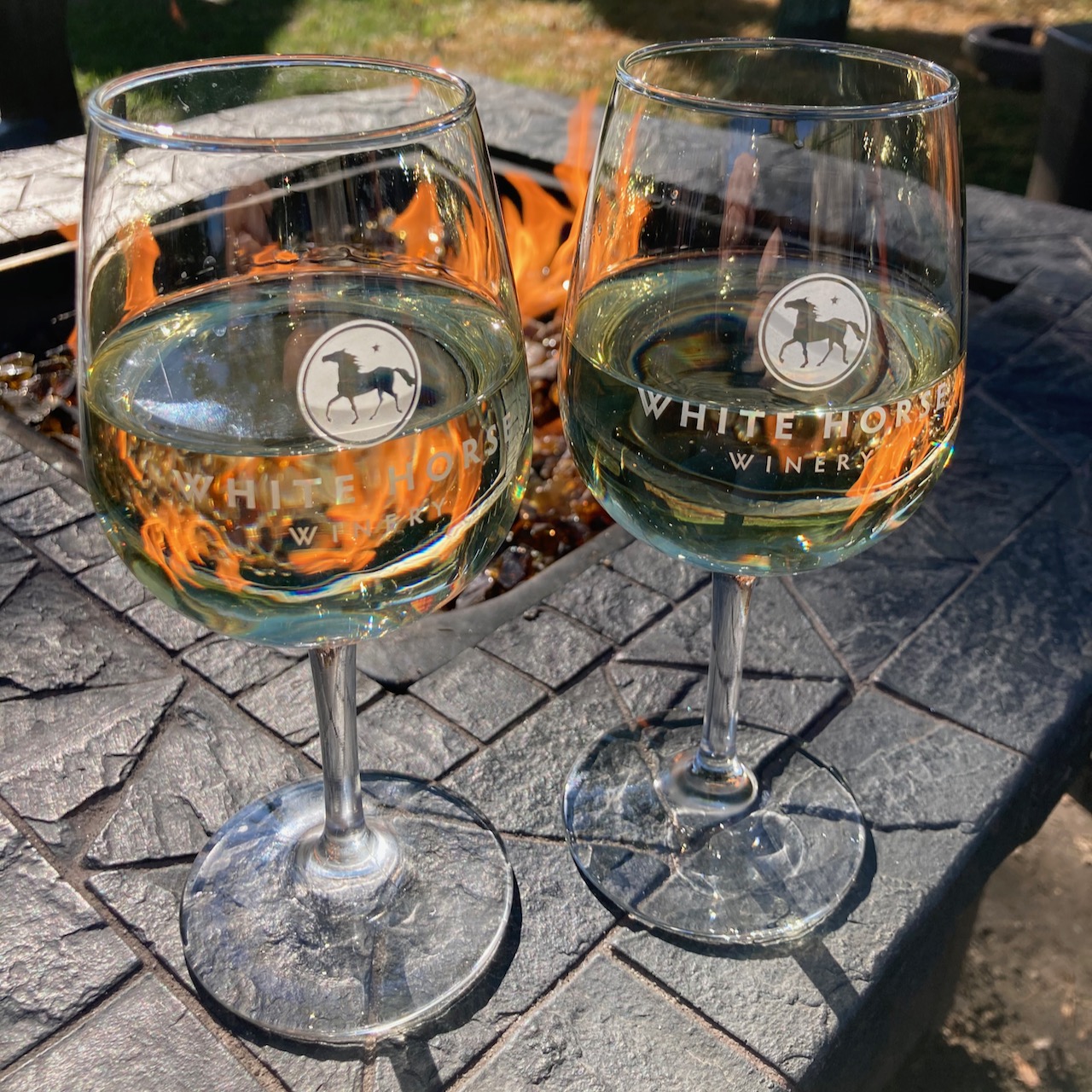 Two glasses of wine in front of fire pit.