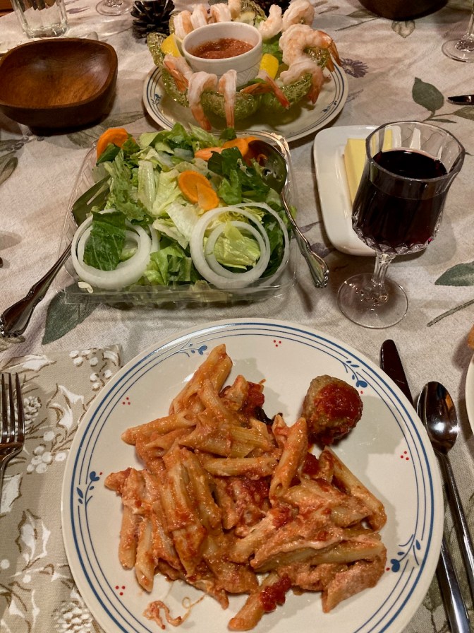 Pasta and meatballs on plate, with glass of wine, tossed salad, and shrimp cocktail on table.