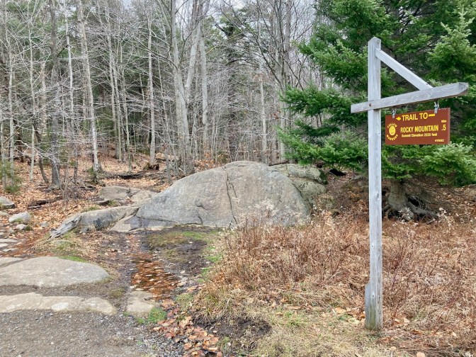 Trailhead sign by entrance to woods that says TRAIL TO ROCKY MOUNTAIN .5 MILES