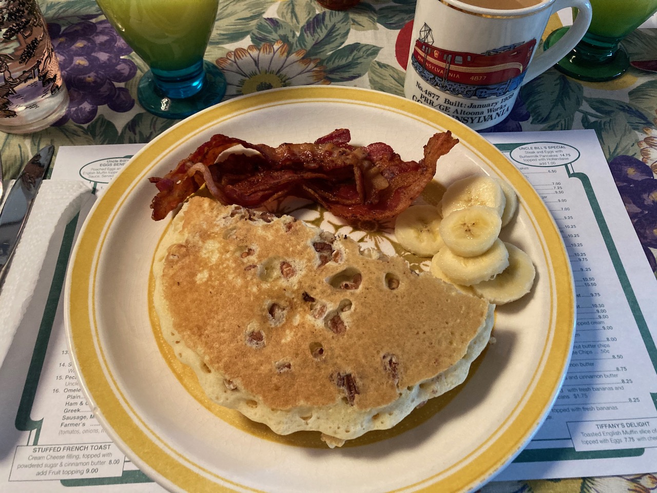 Plate with pancakes, banana slices, and bacon, on a menu placemat.