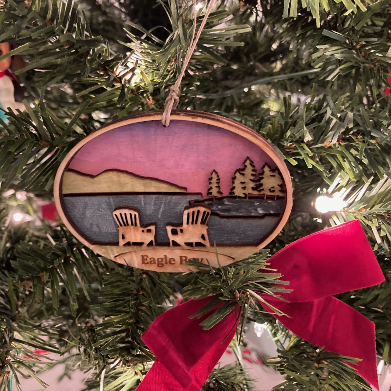 Christmas tree, with ornament in center of image that has two Adirondack chairs overlooking a lake, with the words EAGLE BAY at the bottom.