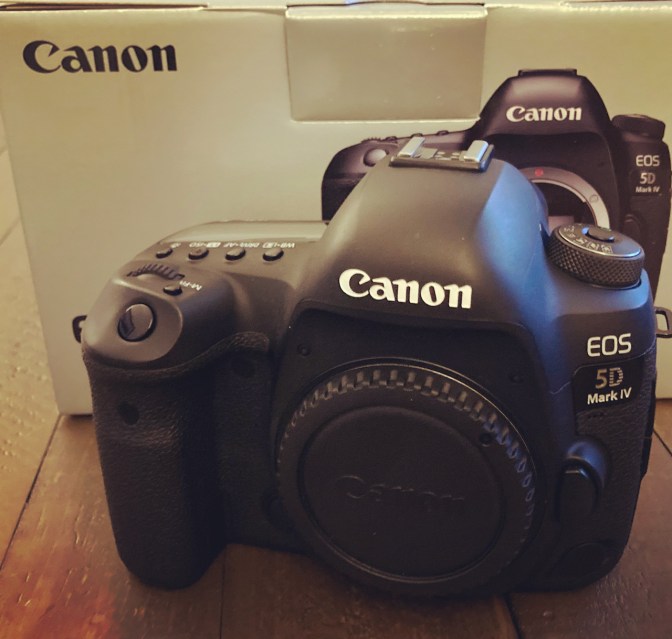 Canon EOS 5D Mark IV camera body on wooden table, with box in background.