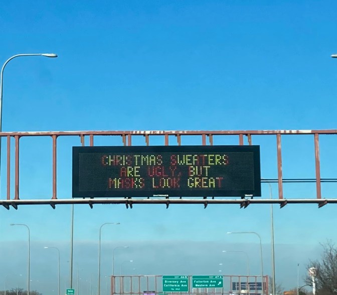 Roadway billboard that says CHRISTMAS SWEATERS ARE UGLY, BUT MASKS LOOK GREAT.