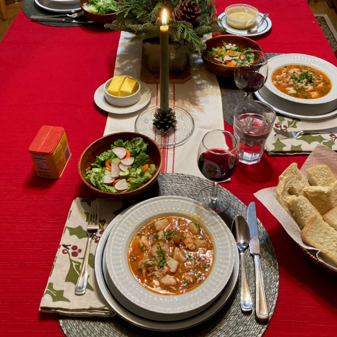 Table with red tablecloth, with seafood soup, salad, and bread on table.