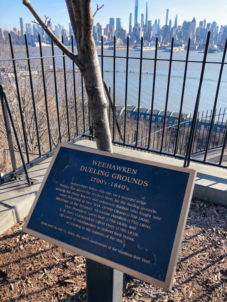Plaque with description of Weehawken Dueling Grounds 1700s - 1840s, with view of Hudson River and Manhattan skyline in distance.