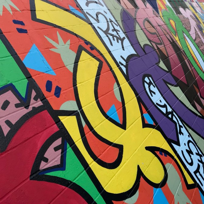 Mural of dancing figures pained on cinderblock wall.