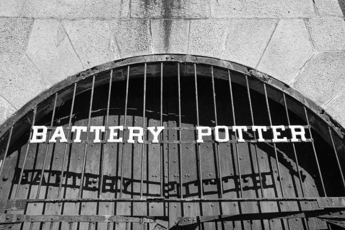 Barred metal doors that say BATTERY POTTER with shadow spelling same words on door.
