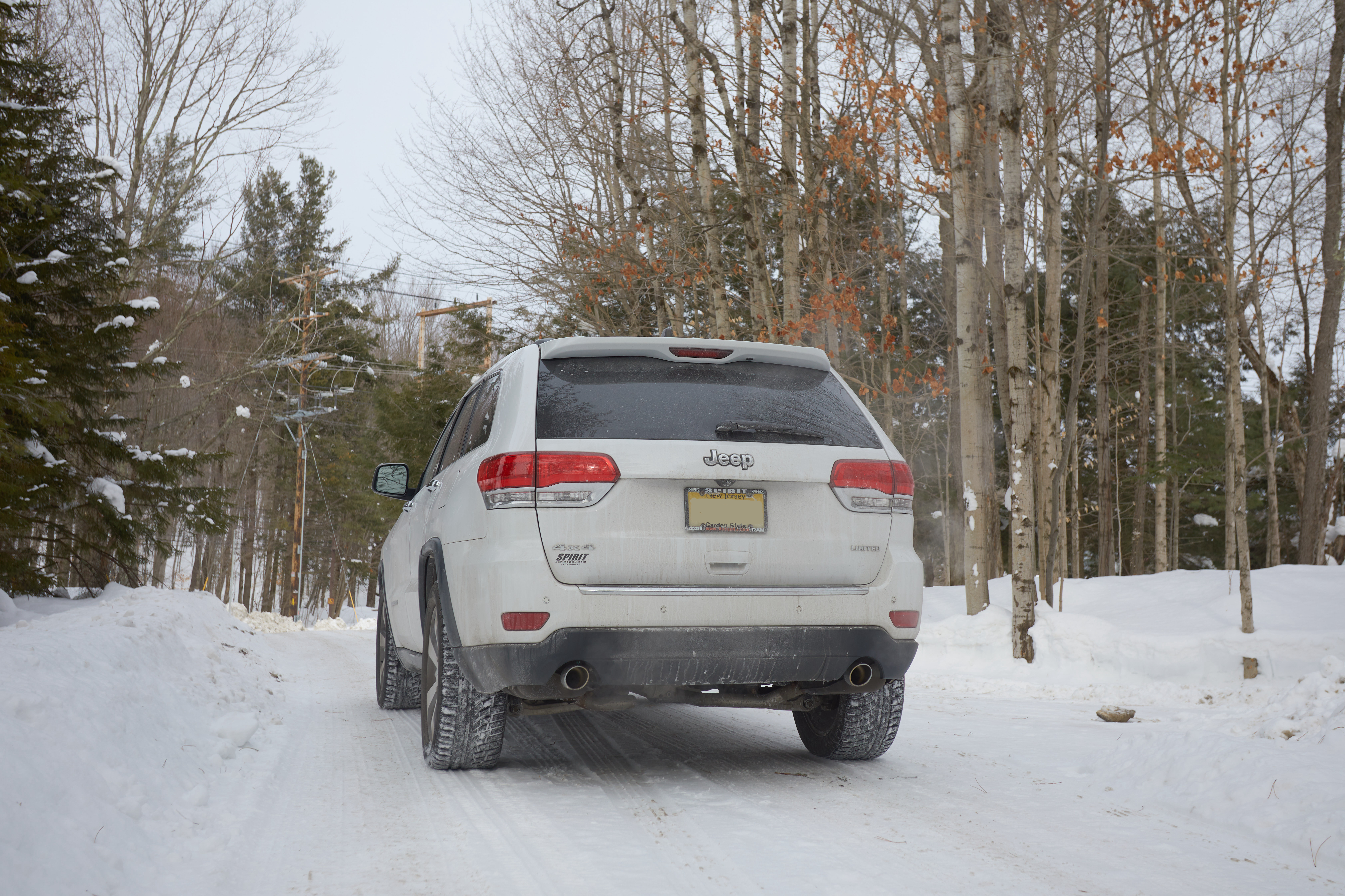 White Jeep Grand Cherokee parked on snow-covered road.