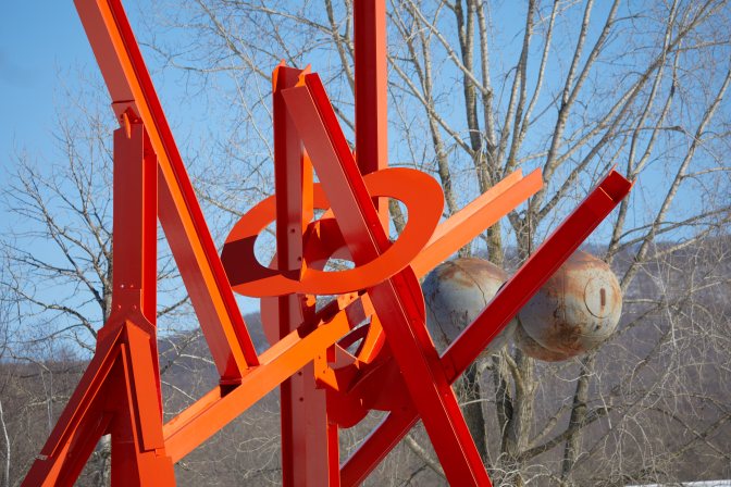 Red metal sculpture with trees in background.