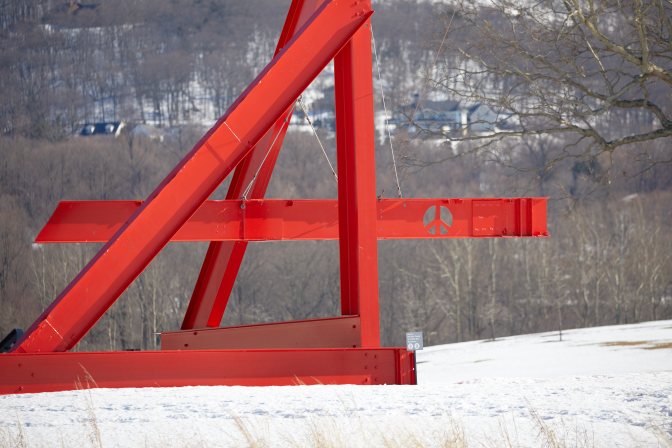 Red structure made of steel girders, with peace symbol on one.