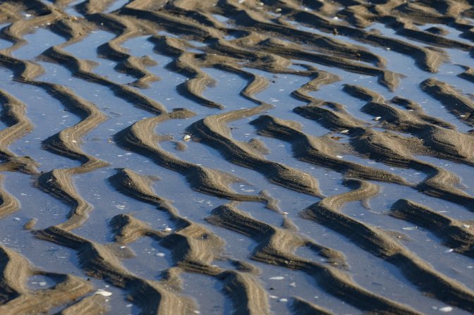 Wavy lines of sand, with water between them.