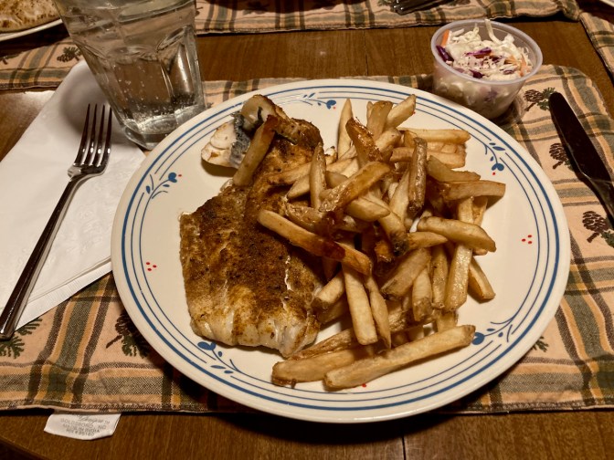 Blackened fish with french fries and coleslaw on plate.