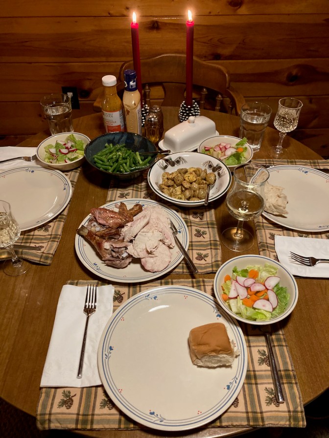 Table with place settings for three people, chicken, roasted potatoes, green beans, and salad.