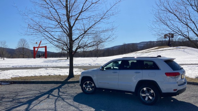 Jeep Grand Cherokee parked in front of field with sculptures.