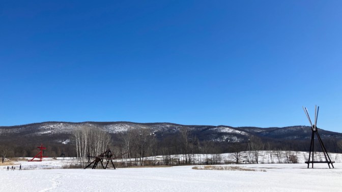 Field with sculptures, with mountains in background.