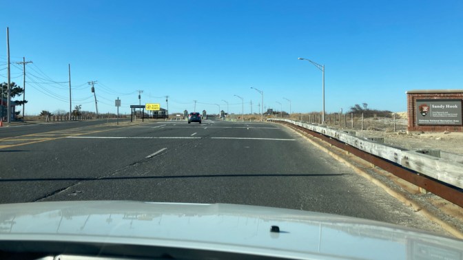 Entrance to Sandy Hook park, with sign on right of road that says SANDY HOOK.