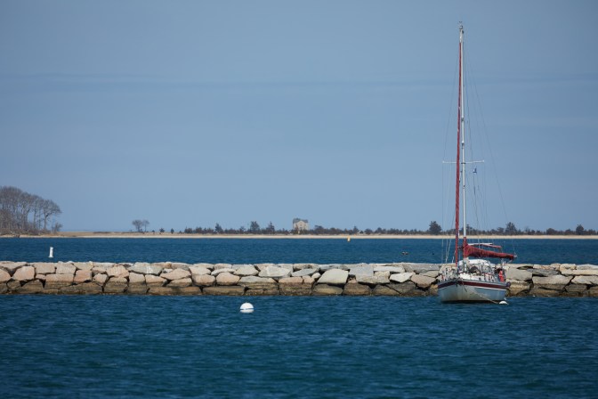 View of Sag Harbor, with sailboat by a jetty and island in distance.