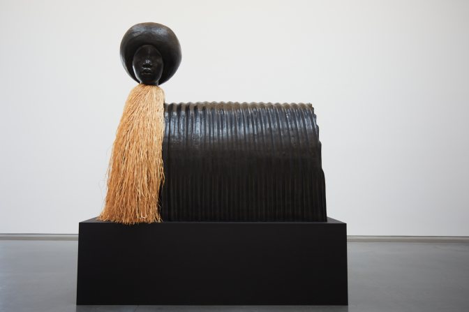Sculpture of woman's head atop stand, with straw body.