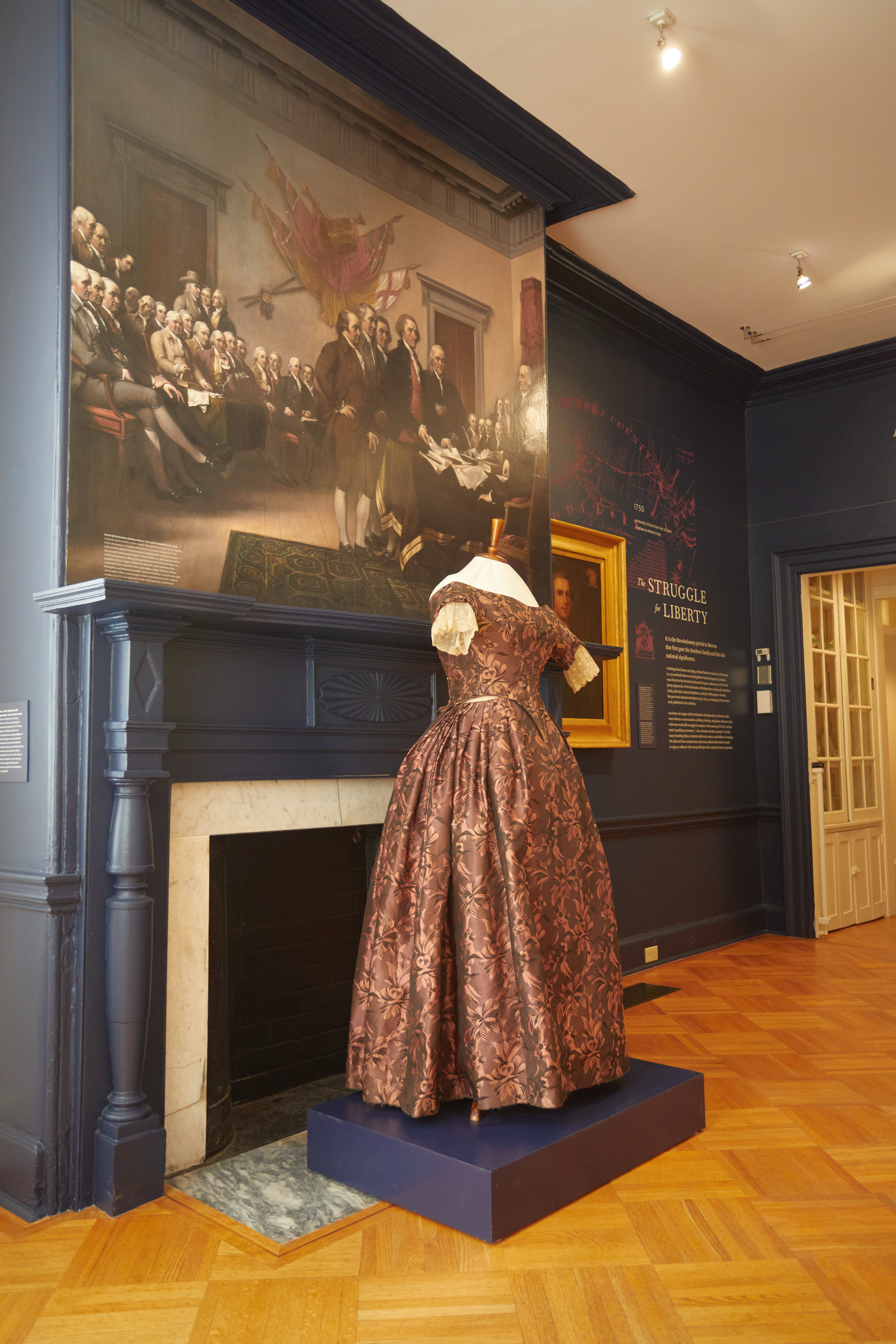 Room with woman's gown on display in front of mural of the signers of the Declaration of Independence.