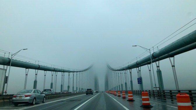 View of Verrazano Narrows Bridge from on bridge, with top structure disappearing into fog.