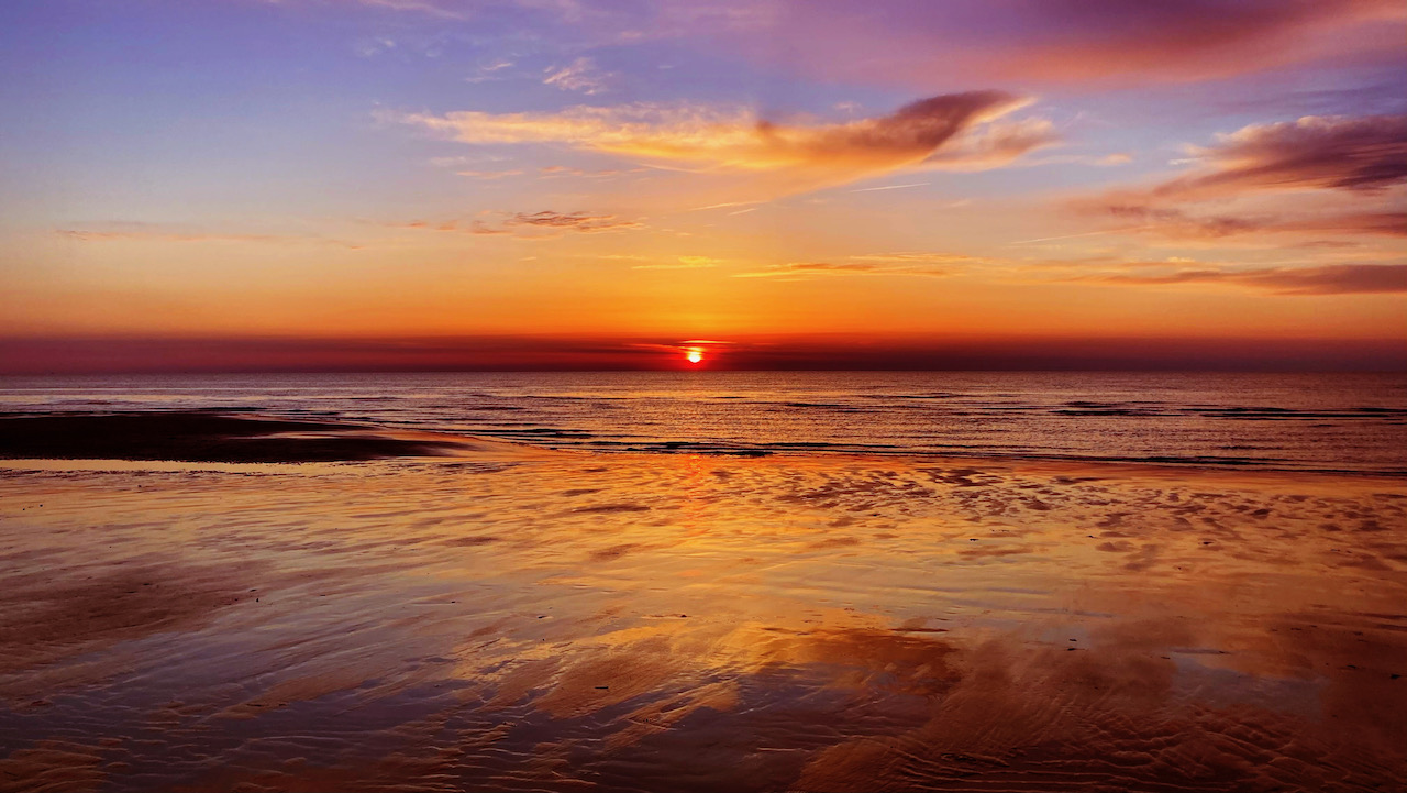 Setting sun over beach, with light reflected in water.