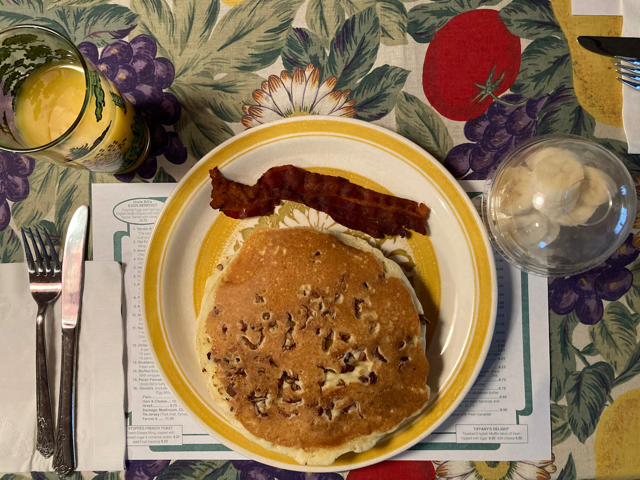 Plate with pancakes and bacon, with a glass of orange juice and a side of banana.