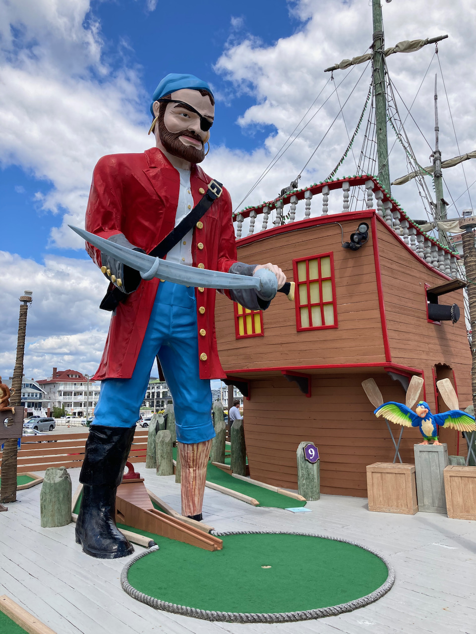 Statue dressed as pirate, standing above miniature gold course hole. A pirate ship is in the background.