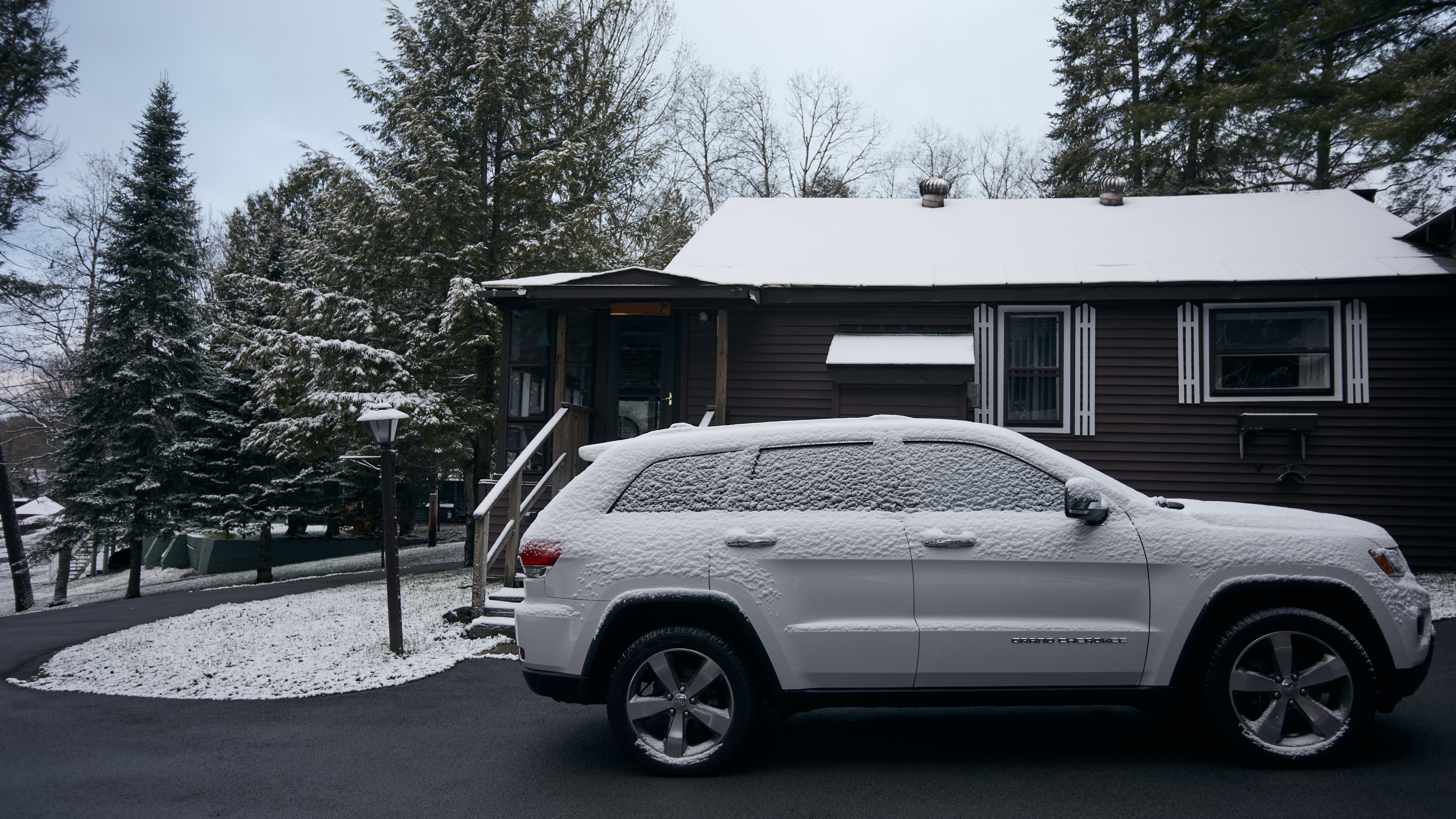 Jeep Grand Cherokee covered in snow, parked in front of house.