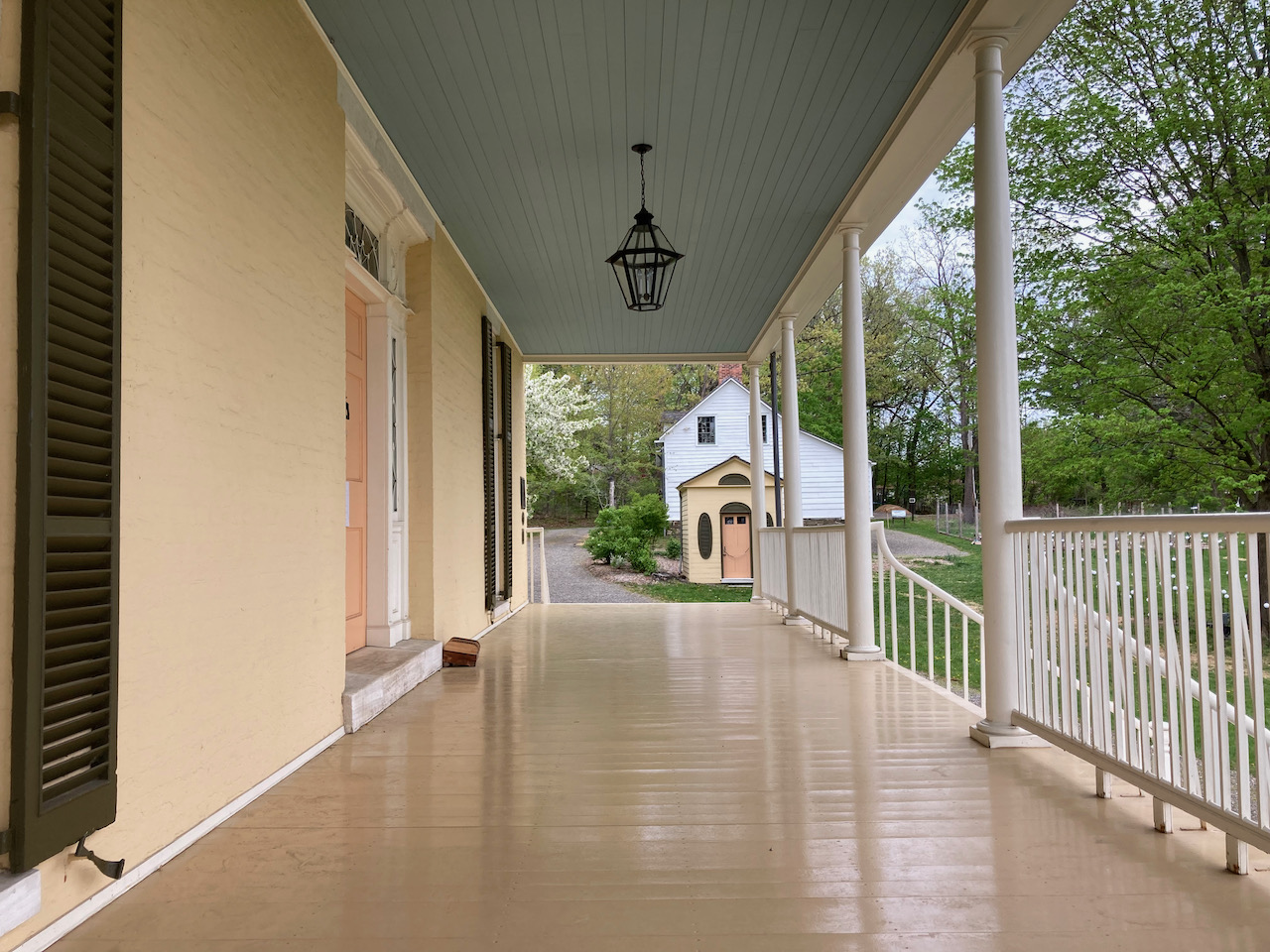 Porch of house, with two smaller buildings in background.
