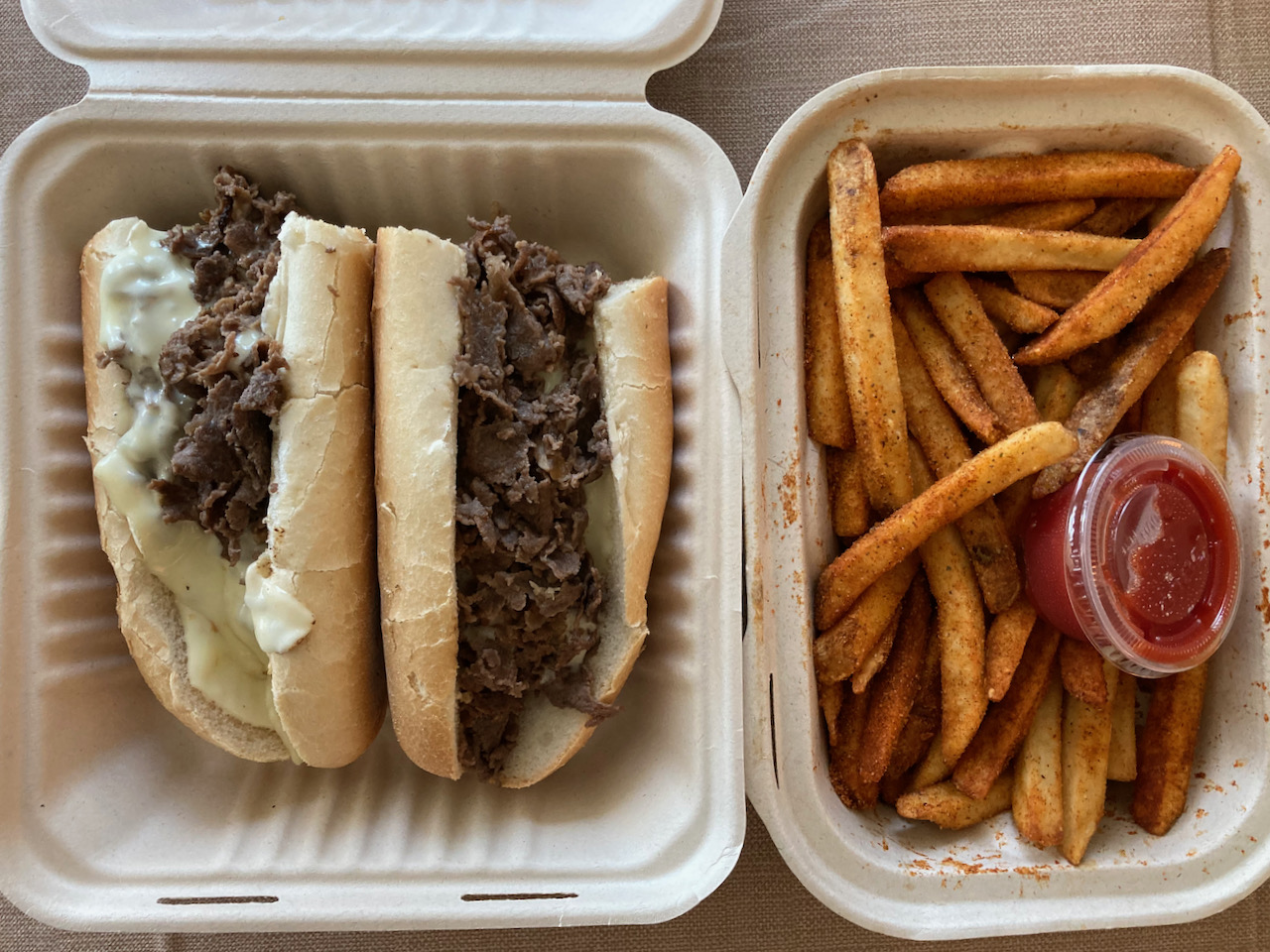 Container with cheesesteak and another container with french fries with Old Bay seasoning.