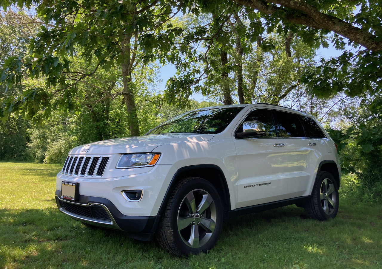 White Jeep Grand Cherokee, parked on grass beneath a tree.