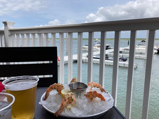 Shrimp cocktail and beverages on table overlooking water.