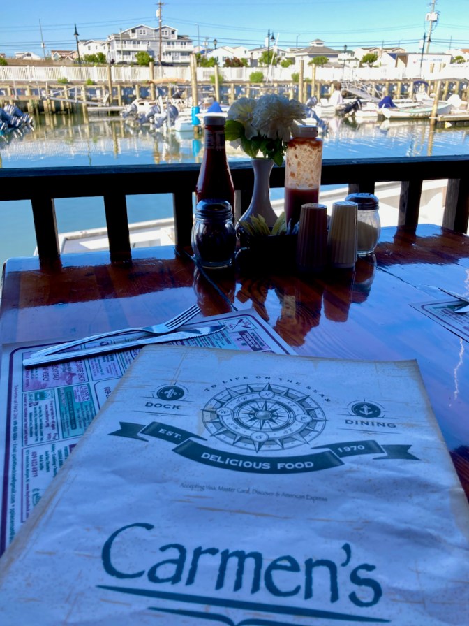 Table with menu for Carmen's, and boats docked in the harbor in the background.