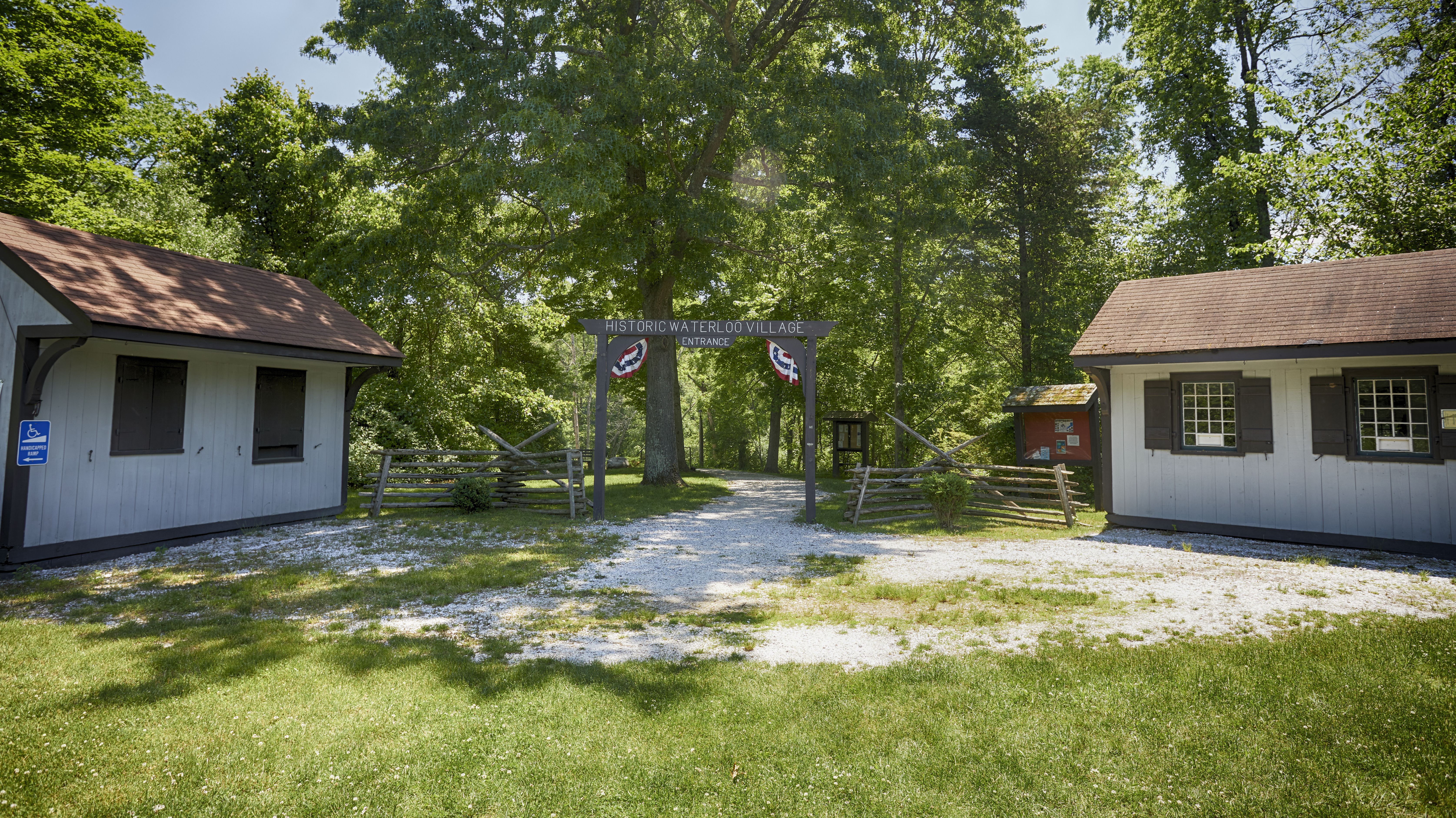 Entrance sign for HISTORIC WATERLOO VILLAGE, with two small buildings on either side of entry gate.