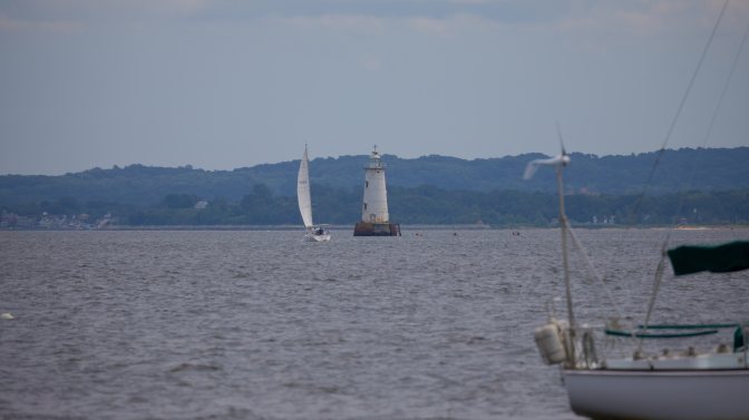 Great Bed Lighthouse with sailboat passing by it in bay.