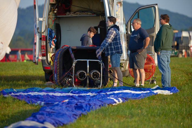Group of people beginning assembly of hot air balloon, including preparing basket and burners.