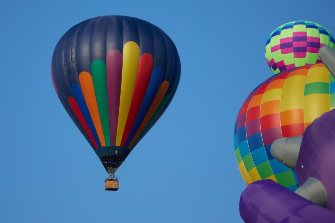 Multi-colored ballon in flight, moving past two balloons still on ground.