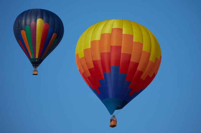 Two multi-colored balloons in sky.