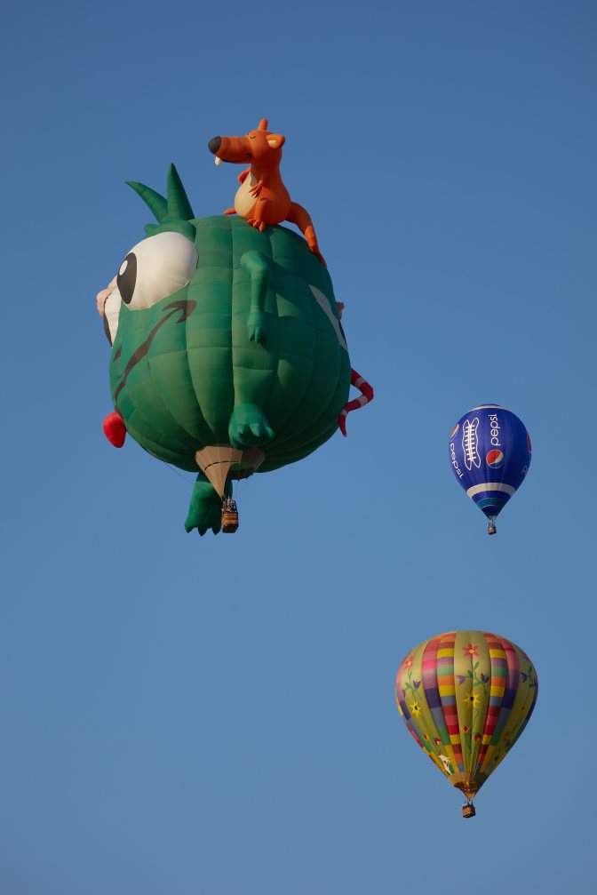 Green monster balloon, blue ballon, and multicolored balloon in sky.