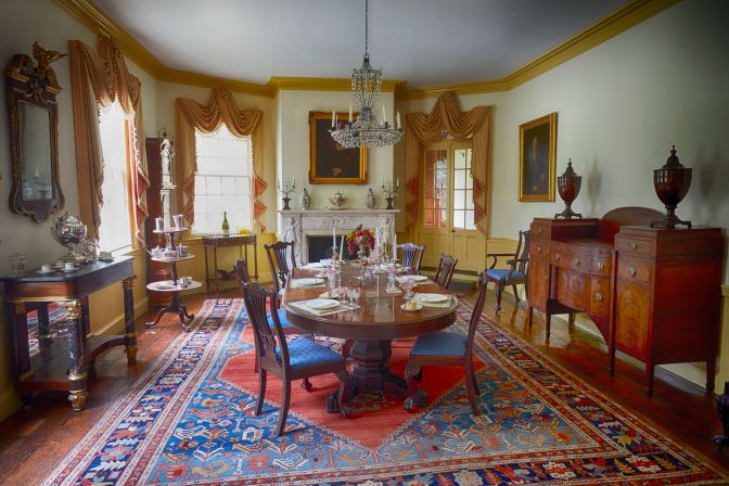 Dining room, with table with six chairs in center of room, chandelier hanging from ceiling, and fireplace along far wall.