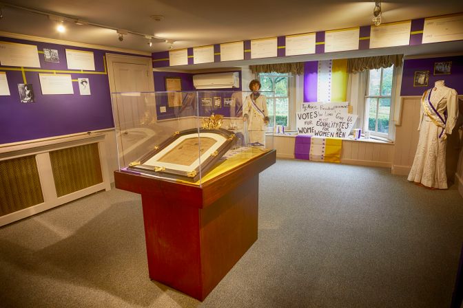 Room-sized display on Suffrage movement, including informational placards and women's suffragette dresses.