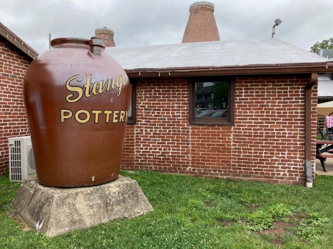 Large pot that says STANGL FACTORY on outside, beside brick building.