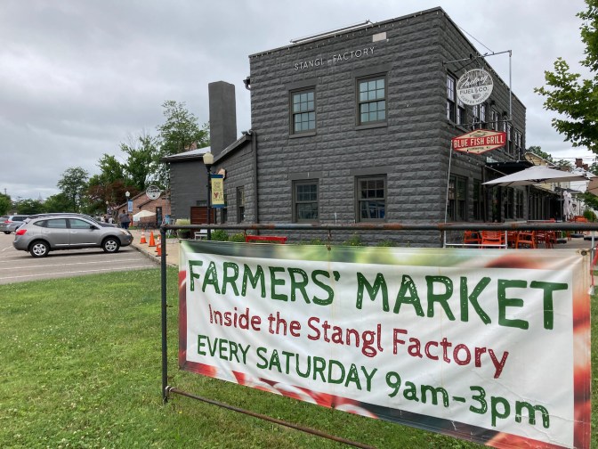 Exterior of Stangl Factory, with sign on lawn that says Farmers' Market - Inside the Stangl Factory Every Saturday 9am - 3pm.