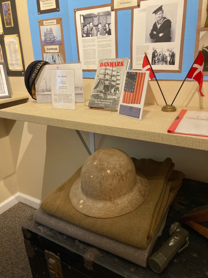 Exhibit on military history, with a WWI helmet, a trunk, and a blanket, as well as photos.