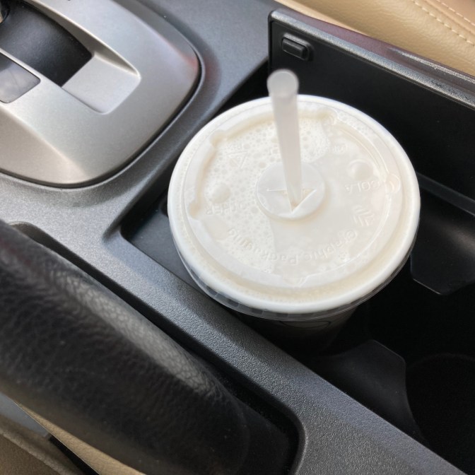White paper cup with plastic lid in car cupholder.