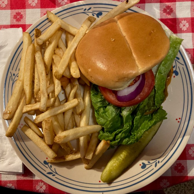 Cheeseburger on plate, with pickle and fries.
