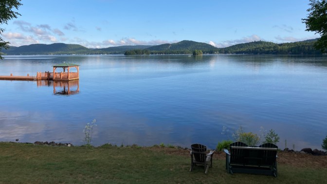 View of Fourth Lake from shore. A pavilion floats in the middle of the lake, connected by a dock to the shore.