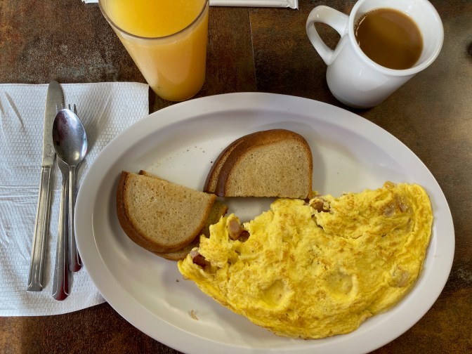 Omelette and toast on plate, with cup of coffee and glass of orange juice on side.